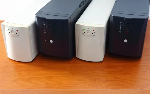 Četiri UPS sustava (dva bijela i dva crna modela) poredana na drvenom stolu, prikazuju različite dizajne kućišta i indikatorskih lampica.