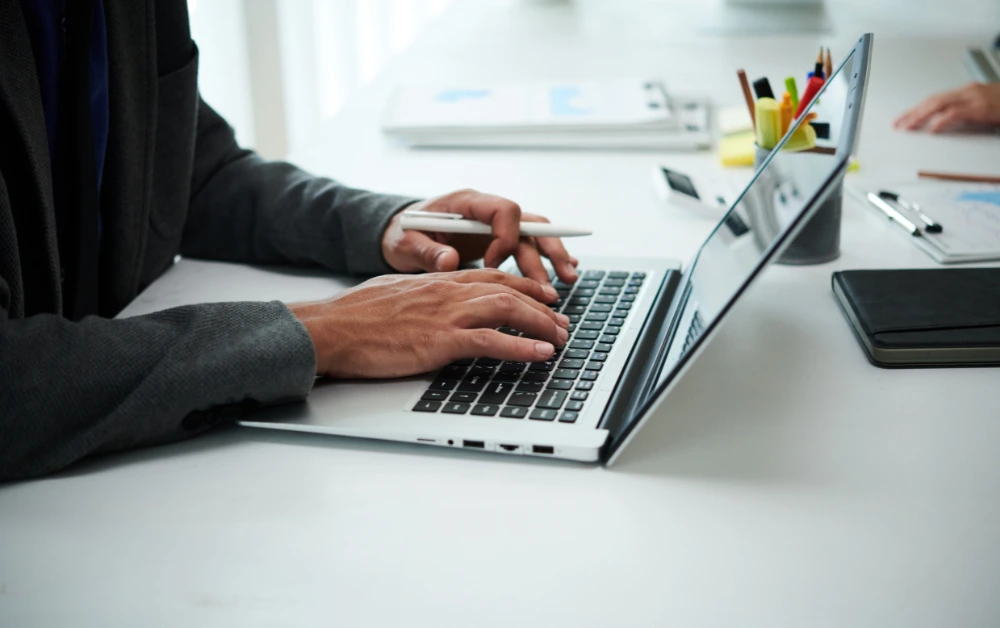 Poslovni čovjek u odijelu koristi prijenosno računalo za rad u svijetlom i moderno uređenom uredskom prostoru.